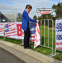 Showing the picture quality of the printed Sports Mesh as used for Baltimore events and public display steel barricades. The young lady is fitting the banner sign to the barricade