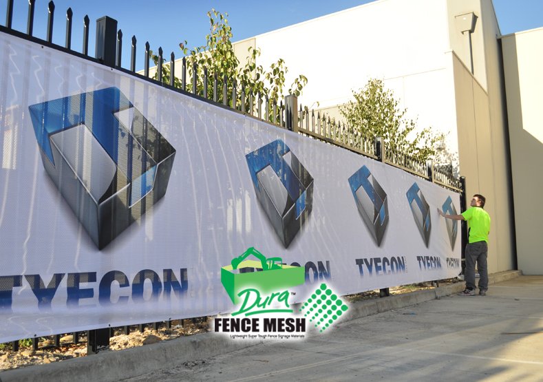 Perspective view of the large outdoor banner on the fence with a worker in the distance. Mesh banners fence.