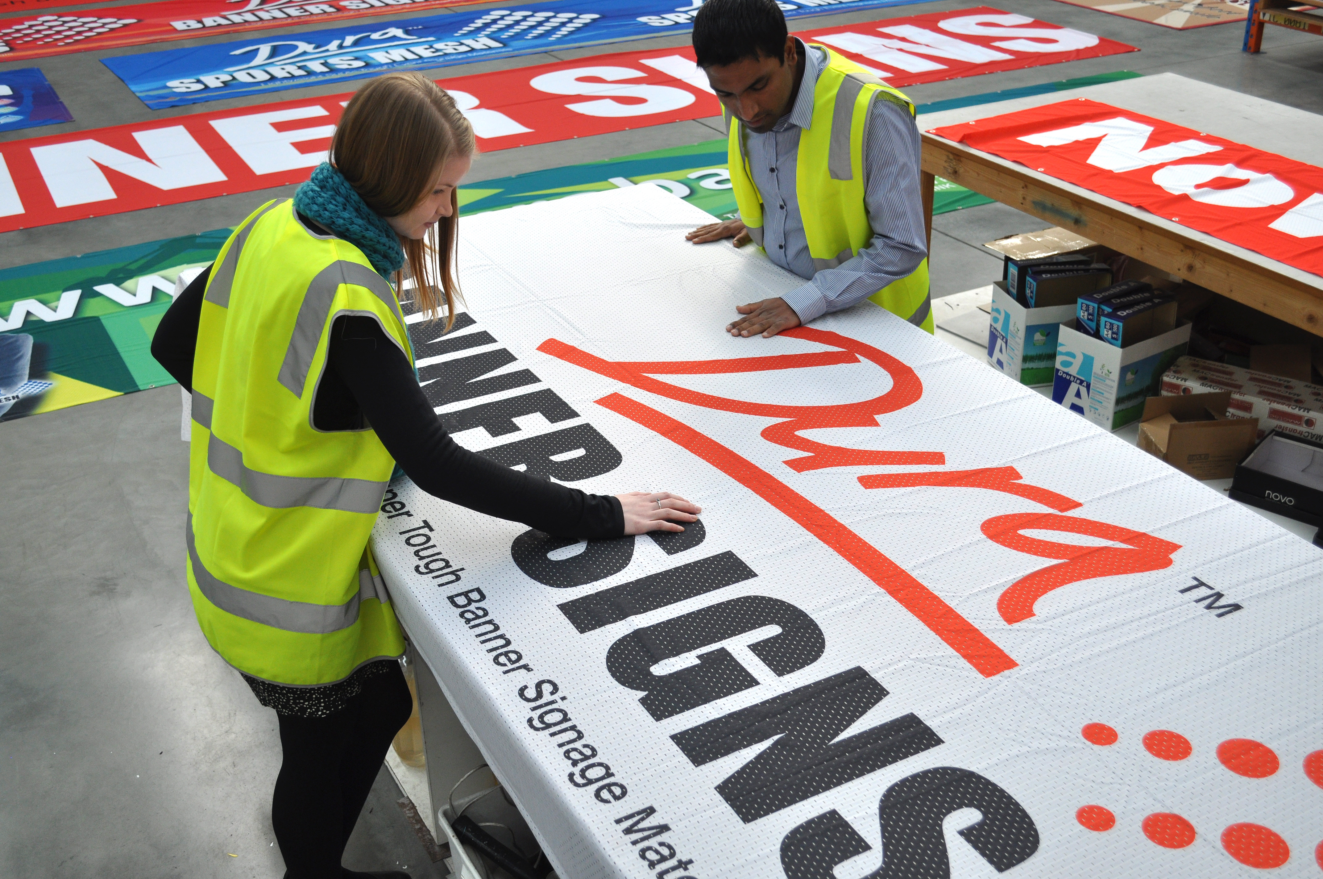 People working inside the banner factory making custom size and custom design banner signage for companies. Material seen is dura 'air' mesh banner.