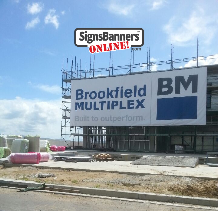 The large vinyl banner sign printed by Signs Banners Online for a construction company was put using zip ties through the holes of the metal grommets. Shows a very big vinyl banner on a new building.