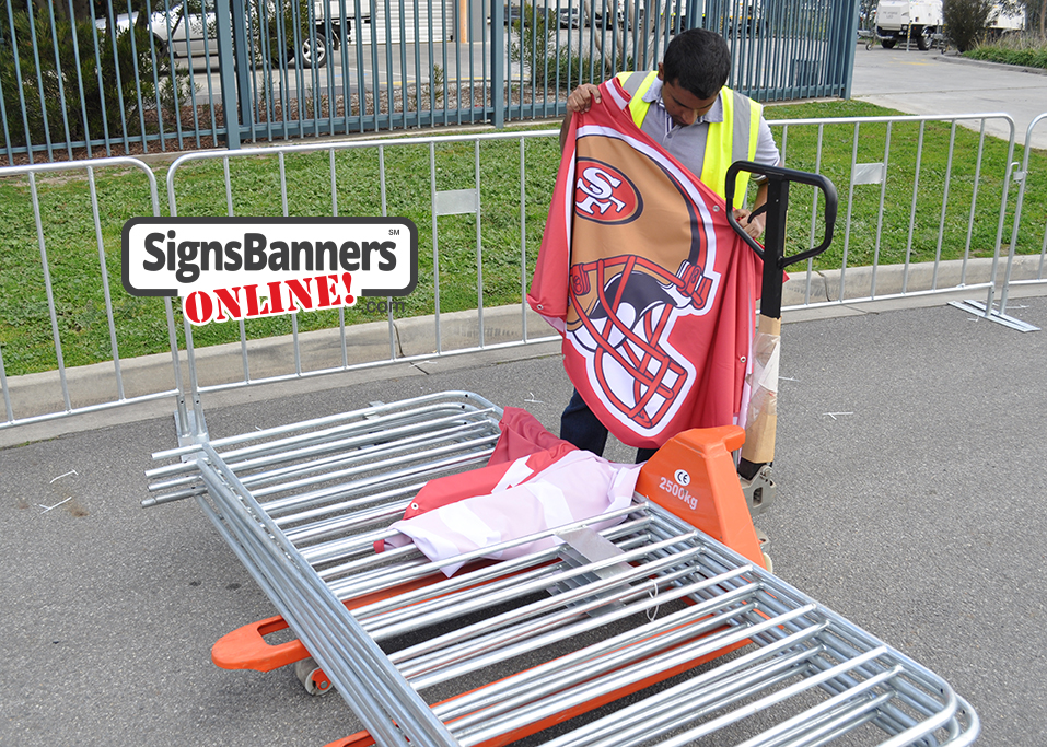 Rental fence erection panels are sitting on the trolley jack lift with fence and banner in the background