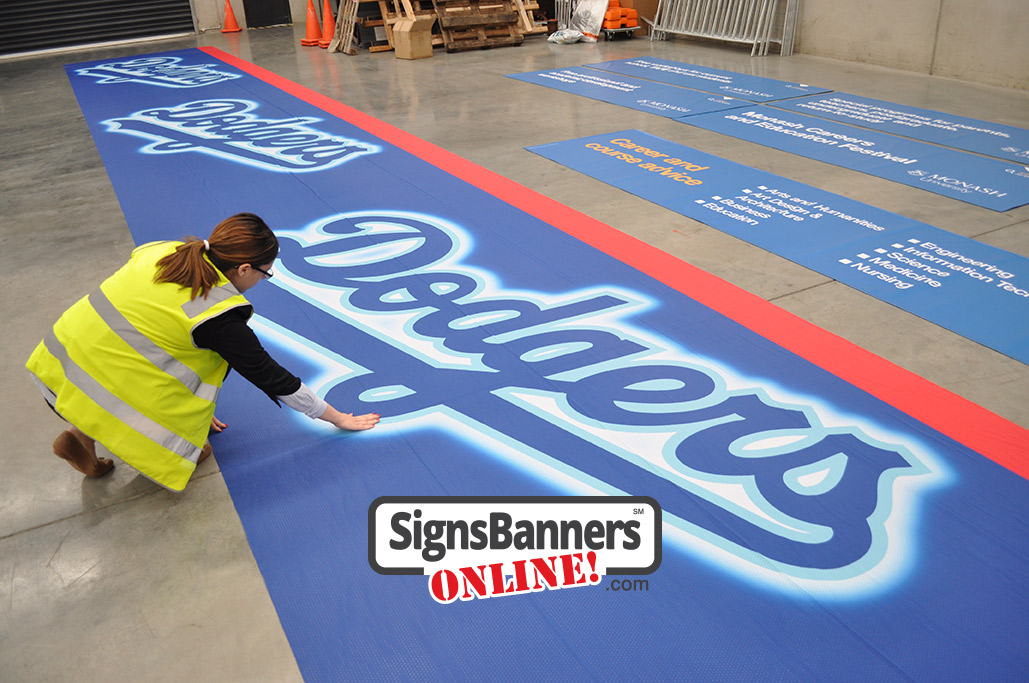 Large repeat logo style outdoor banner sign for a LA Dodgers event. Inspecting the Dodgers banner before ship out for an event. Large banner sign made from lightweight super strong polyester weave with tiny air holes.