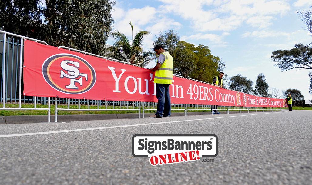 Event graphics team putting up the 49ers banner signs on the temporary event fence covers.