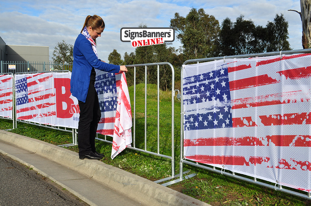 Showing the picture quality of the printed Sports Mesh as used for Baltimore events and public display steel barricades. The young lady is fitting the banner sign to the barricade.