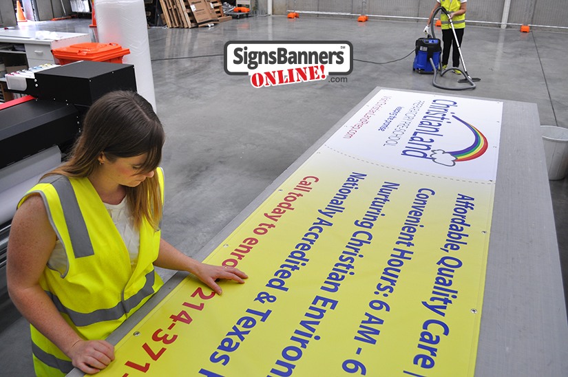 Front; Factory worker making and inspecting banner signs for Dallas Texas 75226; USA; back worker with vacuum cleaning the sign factory floor.